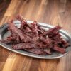A plate of beef jerky on top of a wooden table.