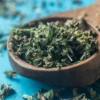 A wooden bowl filled with green leaves on top of a table.