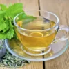 A cup of tea with green leaves on the side.